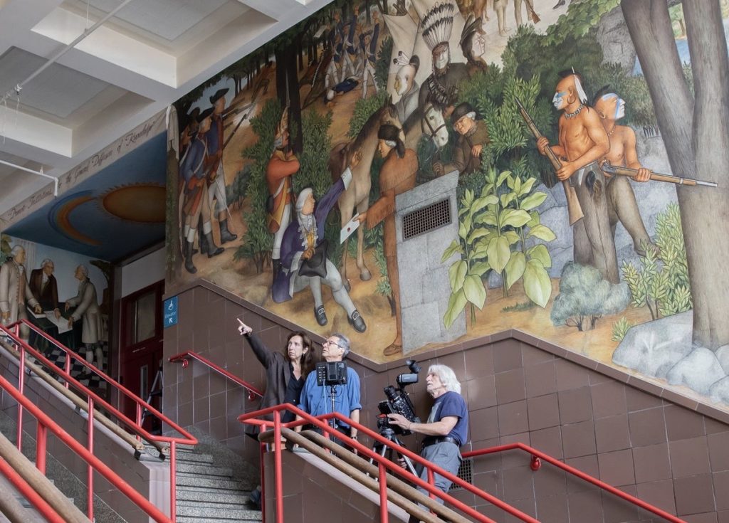 A production still of Deborah Kaufman and Alan Snitow shooting footage on location in front of the controversial mural at George Washington High School in San Francisco